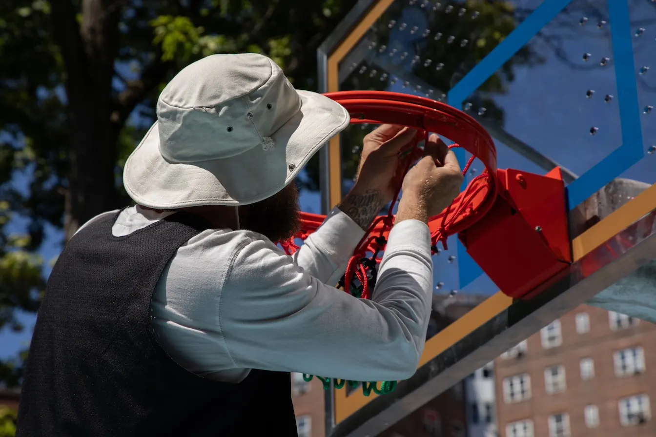 Close view of someone threading a new net onto a bright red rim on a freshly installed glass backboard