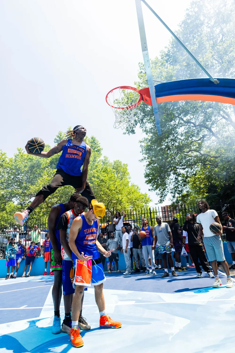 A player in a Hoopbus jersey leaps high above three teammates, ball in hand, on a freshly painted blue court