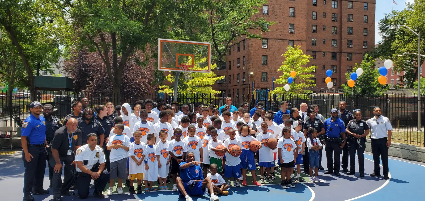 Children in Knicks jerseys gathered on a restored NYCHA court