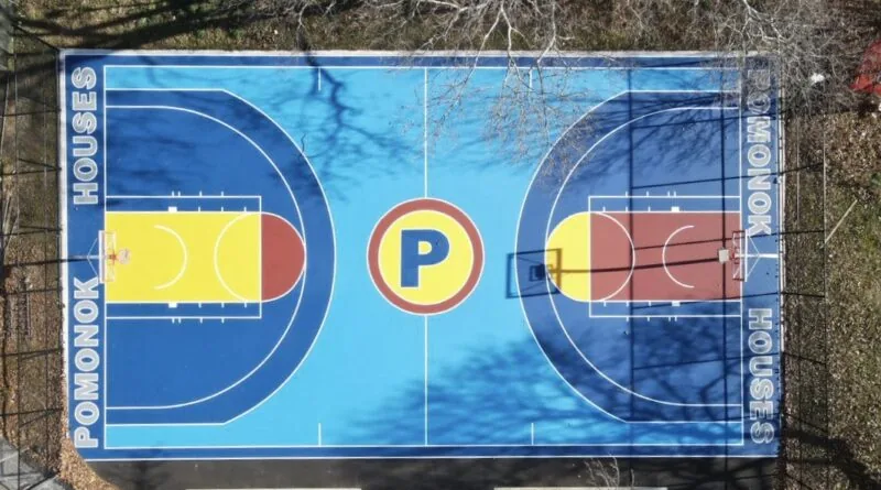 Aerial view of the renovated basketball court at Pomonok Houses, painted blue and yellow with a large P at center court