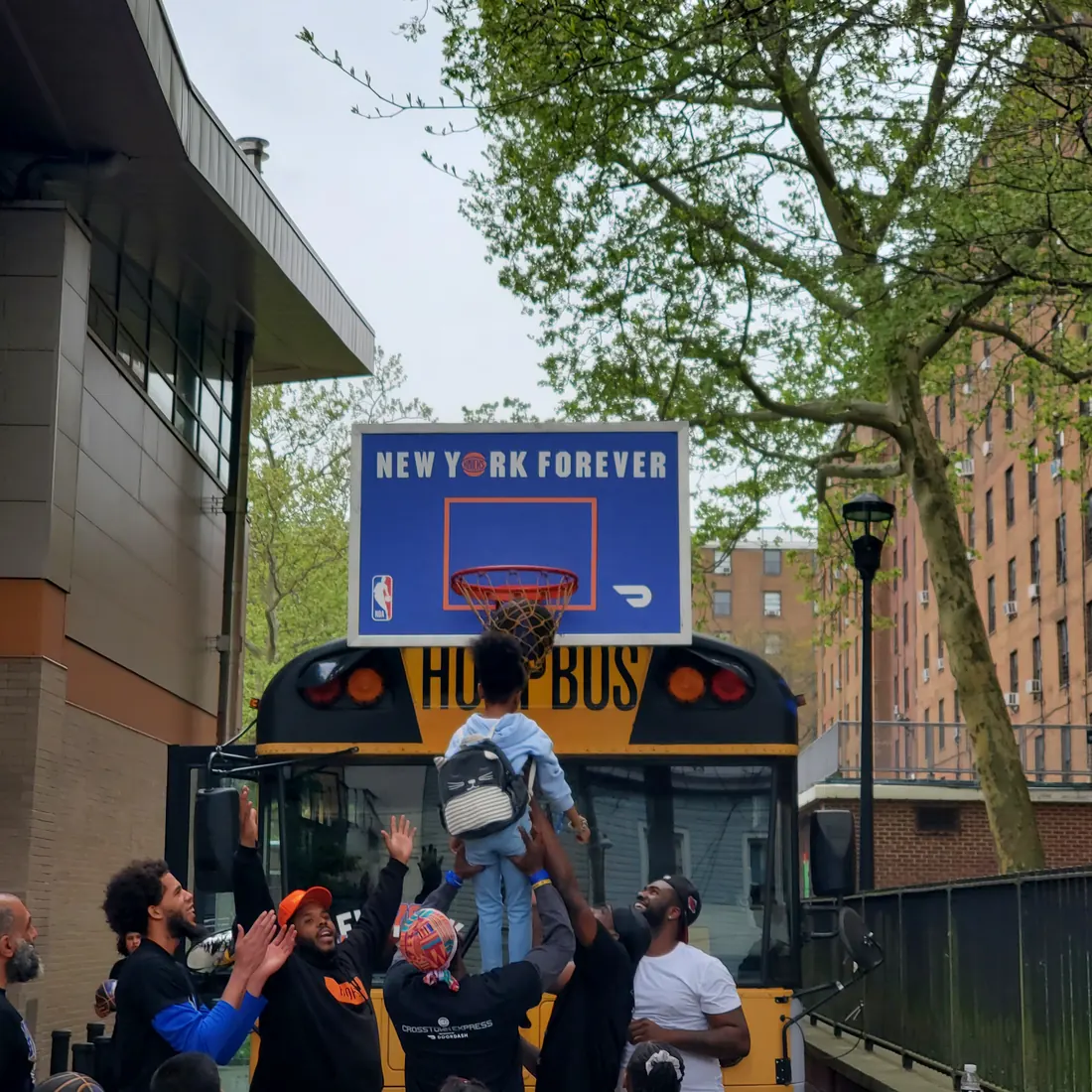 Adults lifting a small child up to dunk a basketball on the hoop mounted to the back of the Hoopbus